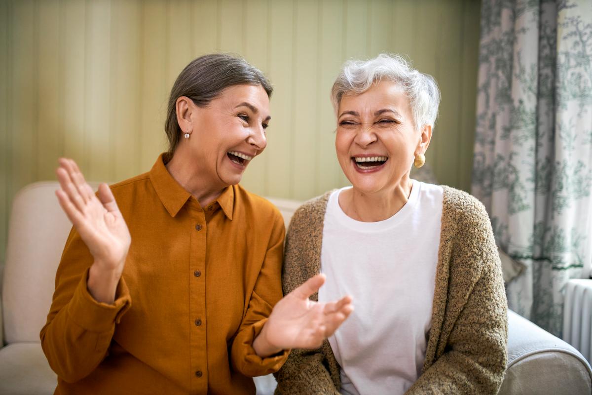 Elderly sisters watching comedy together indoors, laughing.