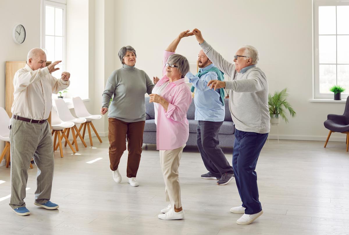 Retirement community. Elderly men and women actively spend time having fun and dancing at party in nursing home.